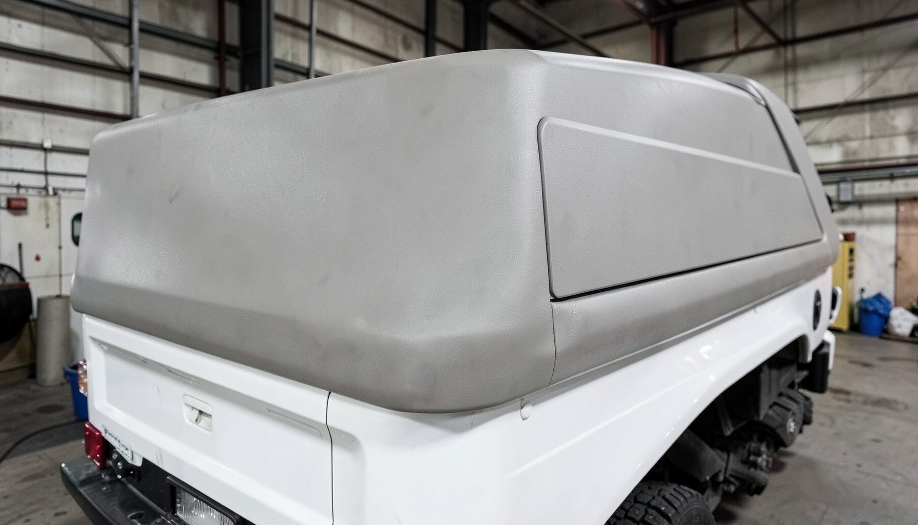 A hard flex tonneau cover on a white work truck, segmented matte panels with subtle texture, industrial setting