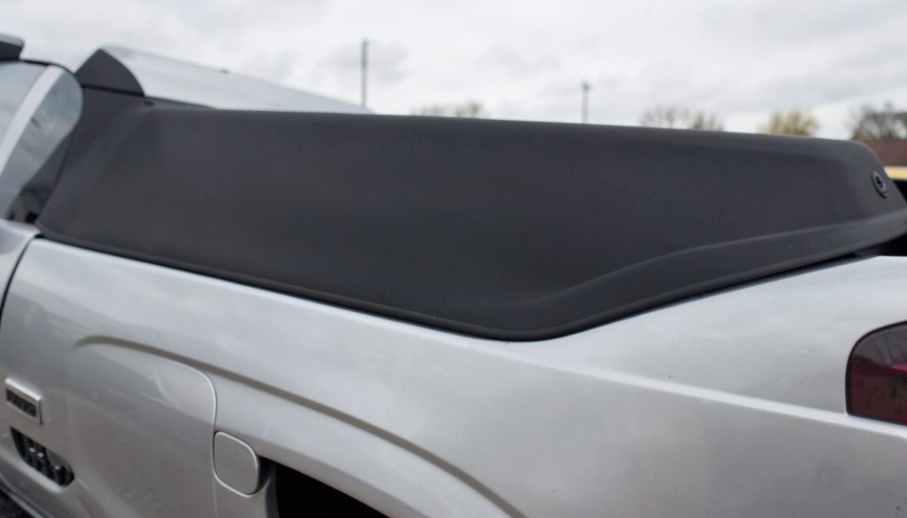 A low-profile hard tonneau cover on a silver pickup, smooth matte black surface reflecting soft overcast light