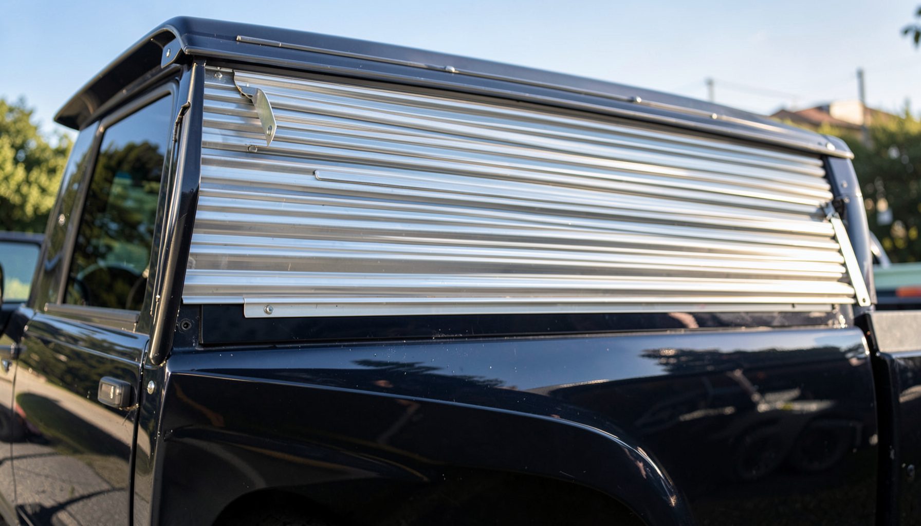A retractable tonneau cover partially open on a dark blue truck, aluminum slats gleaming in afternoon sun